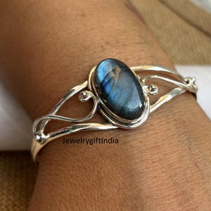 Pode incluir: Um bracelete de prata com uma grande pedra oval de labradorita. O bracelete tem um design delicado e intrincado com um padrão de espiral.