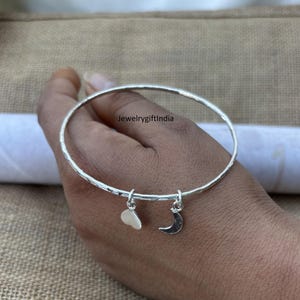 Op de afbeelding: Een zilveren armband met een gehamerde textuur. De armband heeft een hart- en een halve maan bedel. De armband wordt in een hand gehouden, met de tekst "Jewelrygiftindia" zichtbaar.