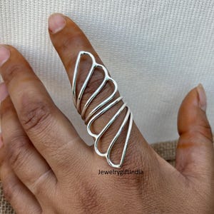 May include: A silver ring with a unique design featuring multiple overlapping heart shapes. The ring is worn on the index finger.