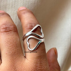 May include: A silver-colored ring with two heart-shaped designs. The ring wraps around the finger, with one heart above and one below. The ring is on a finger against a neutral background. The text "jewelrygiftindia" is visible.