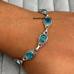 May include: A silver bracelet featuring oval, light blue gemstones. The bracelet has a delicate design with a series of gemstones linked together. The gemstones are set in a silver metal with a textured border. The bracelet is displayed on a person's wrist.