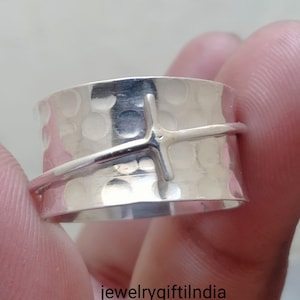 May include: A silver ring with a hammered texture and a cross design. The ring is wide and has a simple, modern style.