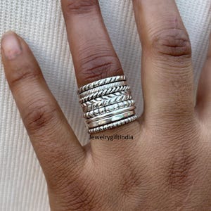 Peut inclure: Une pile de bagues en argent avec différentes textures et motifs. Les bagues sont portées à un doigt.