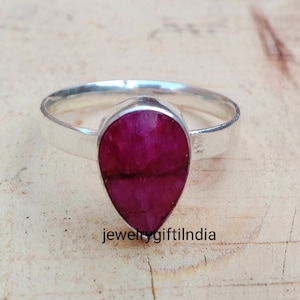 Könnte beinhalten: Ein silberner Ring mit einem birnenförmigen Rubin-Edelstein. Der Rubin ist tiefrot und in einem schlichten Silberband gefasst.