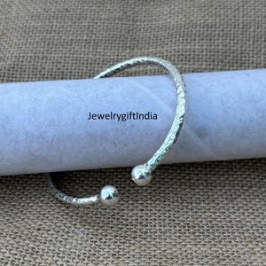 Op de afbeelding: Een zilveren armband met een gehamerde textuur en afgeronde uiteinden. De armband is open en klaar om te dragen.