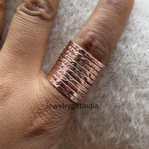 May include: A stack of 10 hammered rose gold rings. The rings are worn on a finger and are a popular style of jewellery.