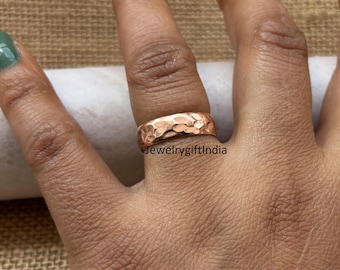 May include: A hammered rose gold band ring. The ring has a textured surface and is worn on a person's finger.