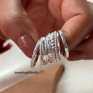 Può includere: Una collezione di anelli d'argento con varie trame, tra cui corda intrecciata, martellata e motivi. Gli anelli sono impilati, mostrando i loro diversi stili. Il testo "JewelrygiftIndia" è visibile in basso.