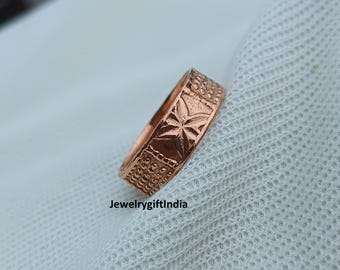 May include: A copper-toned ring with an intricate design. The ring showcases a central star motif and textured edges. The text "JewelrygiftIndia" is present. The ring is set against a white, textured backdrop.