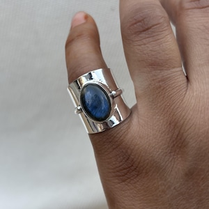 Puede incluir: Un anillo de plata con una gran piedra ovalada de labradorita azul engastada en una banda ancha.