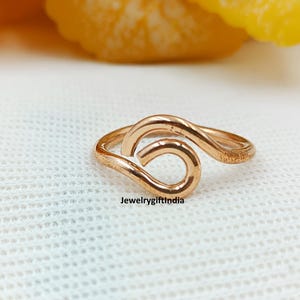 May include: A rose gold ring with a unique, flowing design. The ring features a continuous, looped shape, creating an elegant and modern aesthetic. The text "Jewelrygiftindia" is visible on the ring. The ring is set against a white background.