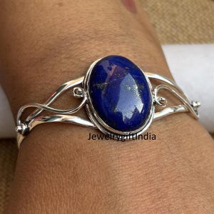 Puede incluir: Un brazalete de plata con una gran piedra ovalada de lapislázuli. El brazalete tiene un diseño delicado e intrincado.