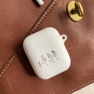 Könnte beinhalten: Weißes Airpods-Case mit einer handgezeichneten Illustration einer dreiköpfigen Familie aus Strichmännchen, die Kronen tragen. Die Zeichnung ist in schwarzer Tinte.
