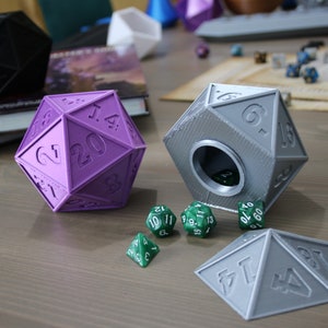 May include: Two 20-sided dice, one purple and one gray, with a hole in the gray die.  The gray die is open and has a green 20-sided die inside.  There are five green 20-sided dice on the table.