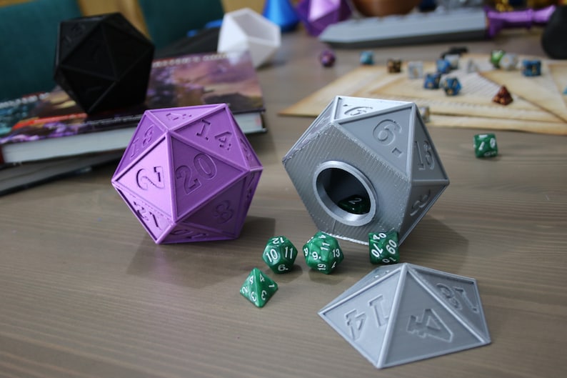 May include: Two 20-sided dice, one purple and one gray, with a hole in the gray die.  The gray die is open and has a green 20-sided die inside.  There are five green 20-sided dice on the table.