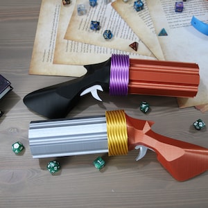 May include: Two 3D printed toy guns with different coloured barrels and handles. The guns are made of plastic and have a futuristic design. The guns are on a wooden surface with dice scattered around them.