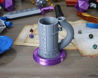 Puede incluir: Una taza de dados gris impresa en 3D con un asa en forma de dragón. La taza tiene una base morada con el texto "This is how I roll" y las palabras "Dice Mug" en el lateral.