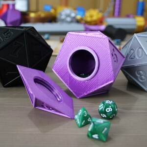 May include: A set of three purple and gray dice with a purple lidded box. The box is open and there are three green dice inside.