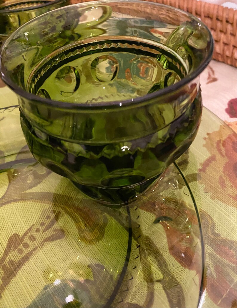 Puede incluir: Un juego de cuatro vasos para beber de vidrio verde con un dise&ntilde;o texturizado. Los vasos tienen una base redonda y un borde ancho.