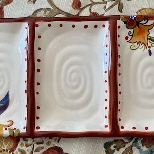May include: A white ceramic serving tray with three divided sections. Each section has a swirl design and is decorated with red dots and colorful floral patterns.