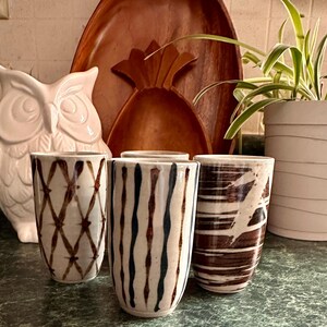 Puede incluir: Cuatro tazas de cer&aacute;mica con diferentes patrones marrones y blancos. Las tazas est&aacute;n sobre una mesa.