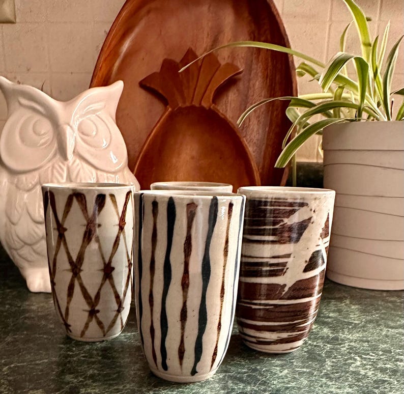 Puede incluir: Cuatro tazas de cer&aacute;mica con diferentes patrones marrones y blancos. Las tazas est&aacute;n sobre una mesa.