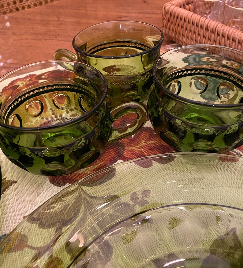Puede incluir: Tres tazas de vidrio verde con un dise&ntilde;o texturizado y un borde festoneado. Las tazas tienen un asa y est&aacute;n sobre una superficie con estampado floral.
