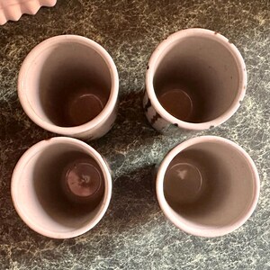 Puede incluir: Cuatro tazas de cer&aacute;mica blanca con esmalte moteado marr&oacute;n y negro. Las tazas est&aacute;n vac&iacute;as y est&aacute;n sobre una superficie marr&oacute;n.