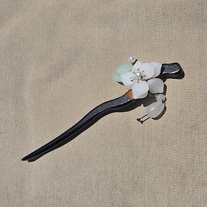 May include: A black wooden hair stick with a decorative floral design. The stick features white flower petals, a pearl accent, and a small bird figurine. The hair accessory is designed for decorative purposes.