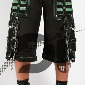 May include: Black cargo shorts with green and white striped panels, featuring multiple straps and silver chains. The shorts have a drawstring waist and are accented with silver hardware.