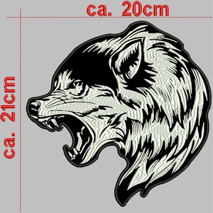 Könnte beinhalten: Schwarz-weiß gestickter Aufnäher mit dem Kopf eines Wolfes, dessen Maul offen ist und die Zähne zeigt. Der Aufnäher ist etwa 20 cm breit und 21 cm hoch.