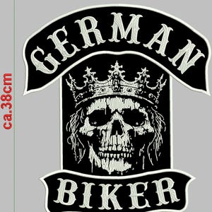 May include: A black and white embroidered patch featuring a crowned skull design. The patch includes the text "GERMAN" above and "BIKER" below the skull. The patch measures approximately 15 inches tall and 12 inches wide.
