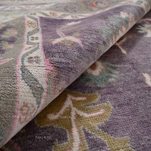 Pode incluir: Close-up de um tapete estampado em roxo, cinza e rosa com um design floral. O tapete tem uma textura macia e felpuda.