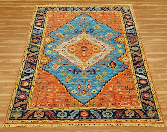 May include: A rectangular rug with an intricate geometric design. The rug features a central diamond shape in turquoise, surrounded by orange and bordered by navy blue. The design includes floral and geometric patterns.