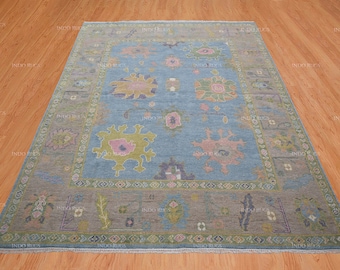 May include: A blue and gray patterned rug with a floral design. The rug has a light blue background with a darker blue border. The floral design is in shades of pink, yellow, and green.