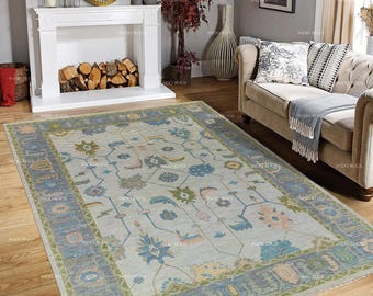May include: A rectangular area rug with a light gray central field and a detailed border. The rug features floral and geometric patterns in shades of blue, green, and peach. The rug is placed on a wooden floor.