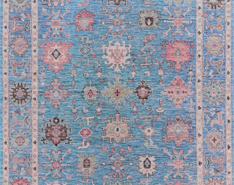 May include: A blue rug with a traditional Persian design. The rug features intricate patterns in shades of pink, green, and brown. The rug has a white border with a repeating pattern.