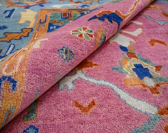 Puede incluir: Primer plano de una alfombra de color rosa y azul con diseños intrincados. La alfombra está doblada por la mitad, revelando el reverso de la tela.