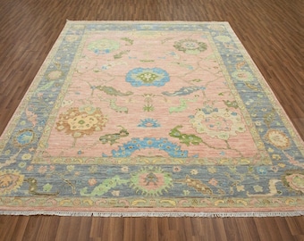 May include: A pink and blue patterned rug with a floral design. The rug has a light blue border with a darker blue inner border. The rug is on a wooden floor.