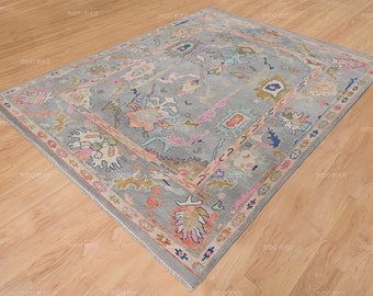 May include: A gray rug with a colorful floral pattern. The rug has a light blue background with pink, orange, and yellow accents. The rug is made of wool and has a hand-knotted construction.