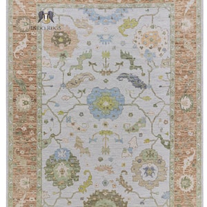 Könnte beinhalten: Ein hellblauer Teppich mit einem floralen Muster in Grün-, Braun- und Blautönen. Der Teppich hat einen braunen Rand mit einem grünen Innenrand.