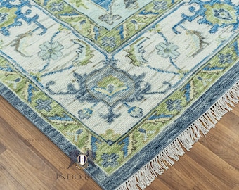 May include: A blue and green patterned rug with a white background and fringe on the edges. The rug has a traditional design with floral motifs.