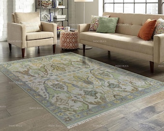 May include: A rectangular area rug with a floral pattern in shades of green, yellow, and blue. The rug has a light-colored background and a border with a fringe. The rug is placed on a hardwood floor.