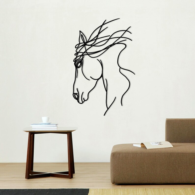 May include: A black line art wall decal of a horse's head with its mane flowing in the wind. The decal is on a white wall above a brown wooden table and a brown couch.