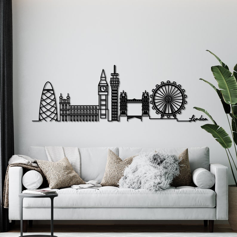 K&ouml;nnte beinhalten: Schwarze und wei&szlig;e Silhouette der Londoner Skyline, einschlie&szlig;lich Big Ben, London Eye und Shard. Die Skyline ist an einer wei&szlig;en Wand &uuml;ber einem grauen Sofa mit Kissen montiert. Das Wort "London" steht in Schwarz unter der Skyline.