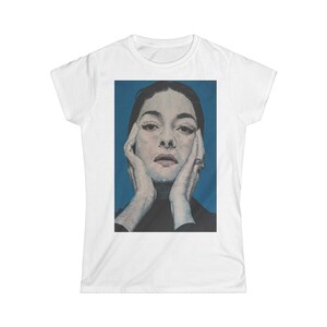 Puede incluir: Un retrato de cerca de una mujer con cabello oscuro y un fondo azul. Lleva un suéter de cuello alto negro y tiene las manos en la cara.