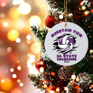 May include: White round Christmas ornament with a purple volleyball with the number 4 on it. The ornament says "Mountain View 3A State Champions 2023".