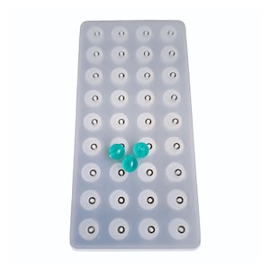 May include: A white silicone mold with 36 round cavities, designed for making small round objects. Three teal-colored round objects are sitting in the mold.