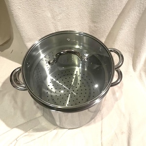 May include: A stainless steel stockpot with a matching steamer insert and a clear glass lid. The pot features two side handles, while the steamer insert has a perforated base for draining. The lid includes a central metal handle and a small vent.
