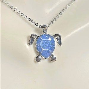 May include: A silver chain necklace with a blue glitter turtle pendant.